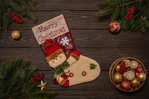 Rustic wooden background decorated with tree branches, gift sock and box of Christmas ornaments