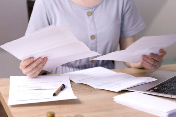 istock A woman sits at a table and holds papers in her hands, looking through them. 1402113282