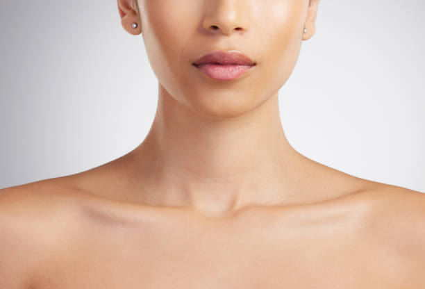 primer plano del cuello y la clavícula perfectos de una hermosa mujer de raza mixta para modelar joyas. el impecable puchero de una mujer hispana con brillo de labios rosa sobre fondo gris de espacio de estudio - women tan perfection naked fotografías e imágenes de stock