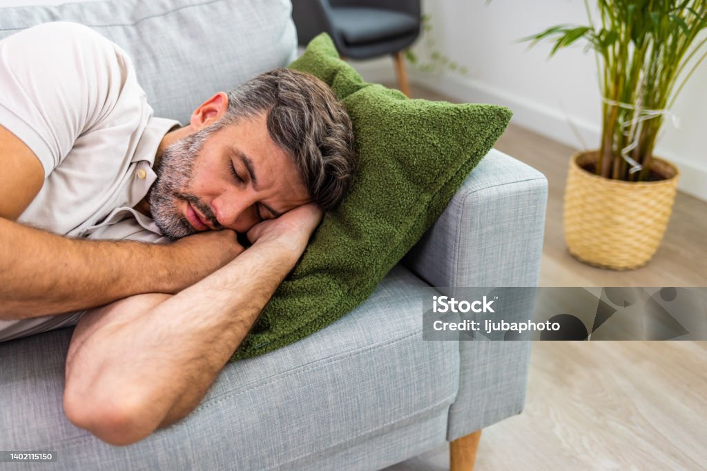 Exhausted young man came home after work flopped down on sofa Shot of a man relaxing on the sofa at home 35-39 Years Stock Photo