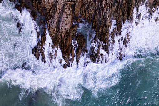 Aerial view Drone camera top down of seashore rocks in a blue ocean Turquoise sea surface Amazing sea waves crashing on rocks seascape. High quality image of sea waves in Phuket Thailand