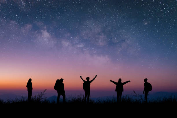 silhouette gruppe von jungen reisenden und rucksacktouristen beobachtete den stern und die milchstraße auf dem gipfel des berges mit dämmerungshimmel. er reiste gerne und war erfolgreich, als er den gipfel erreichte. - milky way star galaxy space stock-fotos und bilder