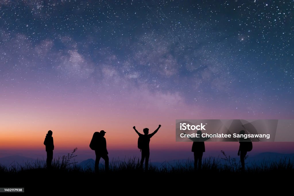Silhouette group of young traveler and backpacker watched the star and milky way on top of the mountain with twilight sky. He enjoyed traveling and was successful when he reached the summit. Astronomy Stock Photo