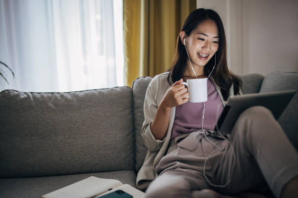istock Young woman sitting on sofa at home using digital tablet with headphones on and working 1402118710