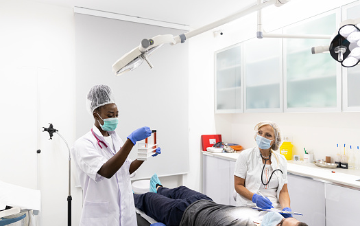 Group portrait of two people, man dentist making treatment in modern clinic for woman. Medical concept photography indoors for dentistry. Dental office, doctor working in clinic with patient.