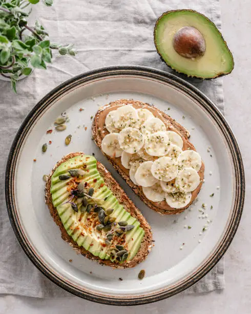 Overhead view of a ceramic plate with avocado toast and peanut butter banana toast