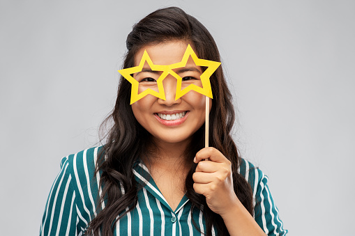 party props, photo booth and people concept - happy asian young woman with big glasses in shape of stars over grey background