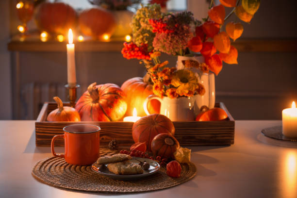 orange cup of tea and autumn decor with pumpkins, flowers and burning candles on table stock photo