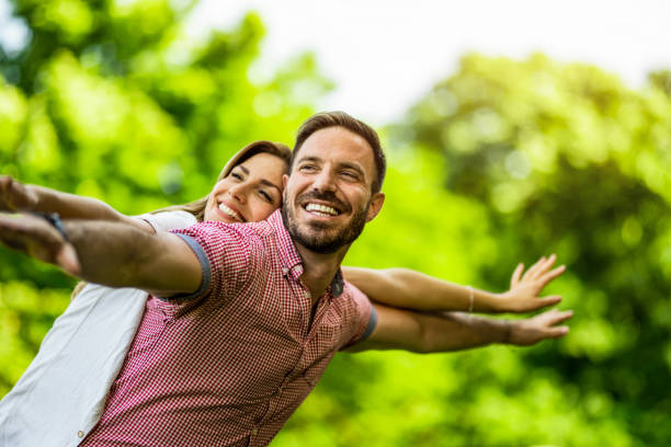 Cheerful young couple standing with arms outstretched in the park on beautiful spring day.