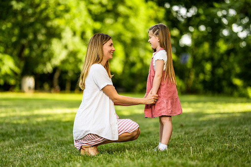 Happy young woman talking with her little girl while holding hands on spring day in nature.