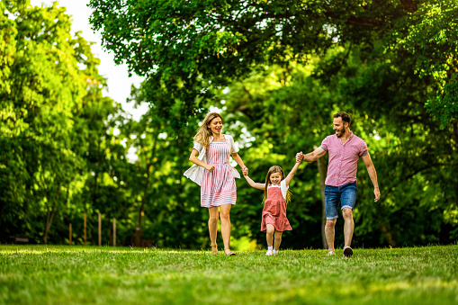 Playful parents having fun with their girl while holding hands and running during spring day in nature.