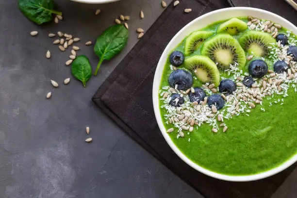 Breakfast green smoothie bowl with kiwi, blueberries and sunflower seeds on gray concrete background. Top view.