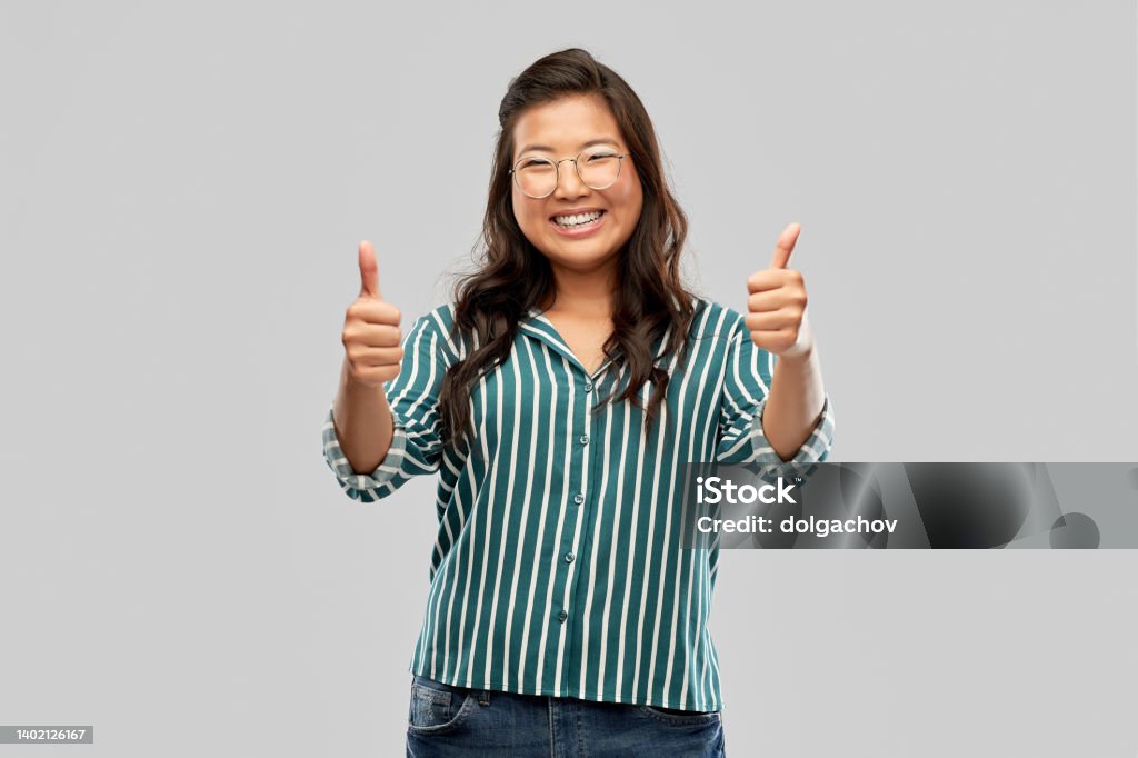 happy asian woman in glasses showing thumbs up people, education and school concept - happy asian woman in glasses or student showing thumbs up over grey background Nerd Stock Photo