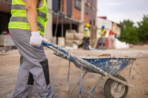 At the construction site, Caucasian female construction worker, pushing the cart with sand