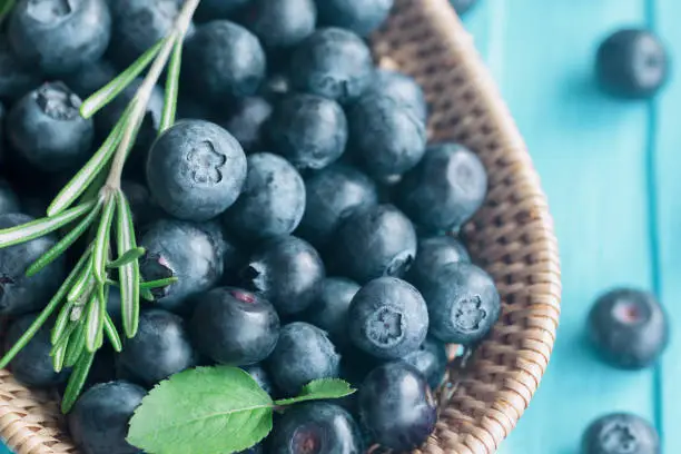 Close up fresh ripe wild blueberries in wooden basket on blue wood table in top view with copy space for background. Blueberry is antioxidant food and vitamin C. Healthy and delicious fruits concept.
