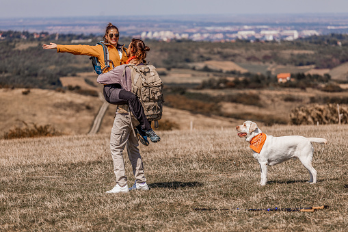 Young man and woman in sports clothes hiking and walking with their playful retriever while exploring nature and enjoying time together