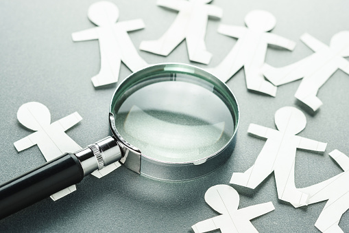 Magnifying glass on many paper human dolls, man management, human resources analytics, searching the right man for a business, recruitment concept