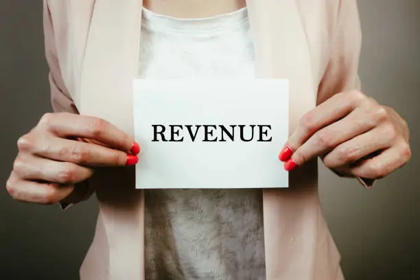 Photo of Businesswoman holding sheet of paper with word revenue. Business and economy concept