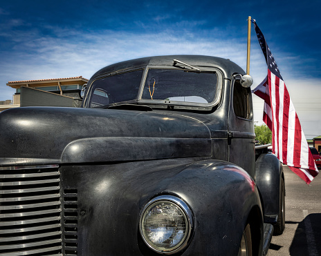 A black pickup truck from the early 1940s, proudly flying an American flag, at a car meet in El Paso, Texas.