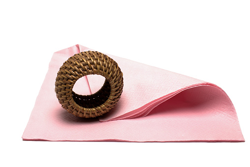 Close up of pink napkin with standing braided wooden straw serviette ring on it on white background
