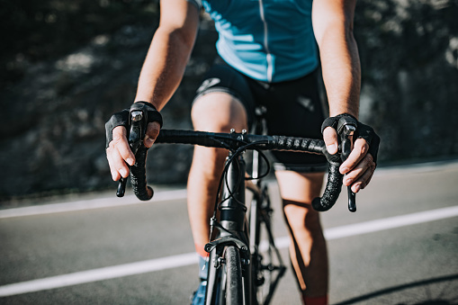 Close up of a young man's hands on a bicycle's handlebar on a rural empty road