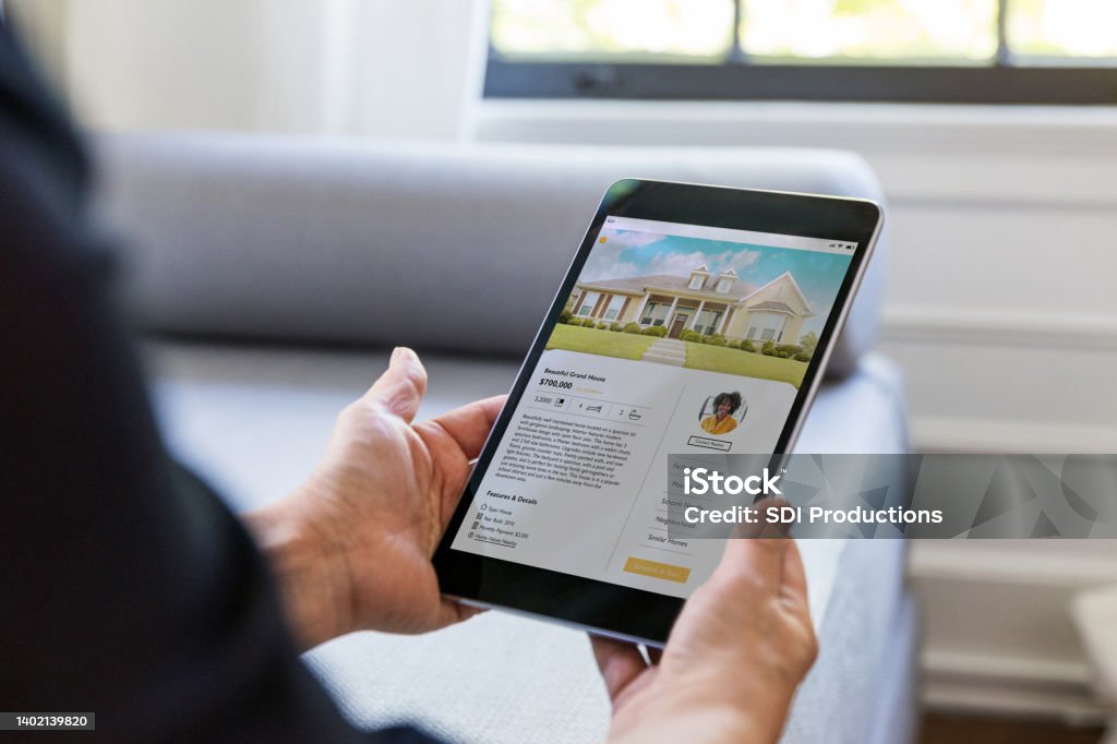 Unrecognizable person looks for home using mobile app An unrecognizable man uses a real estate mobile app in his search for a new home. An exterior photo of the home is on digital tablet's screen. Real Estate Stock Photo