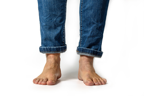 Closeup of unrecognizable young caucasian man feet and wearing denim jeans pants isolated on white background