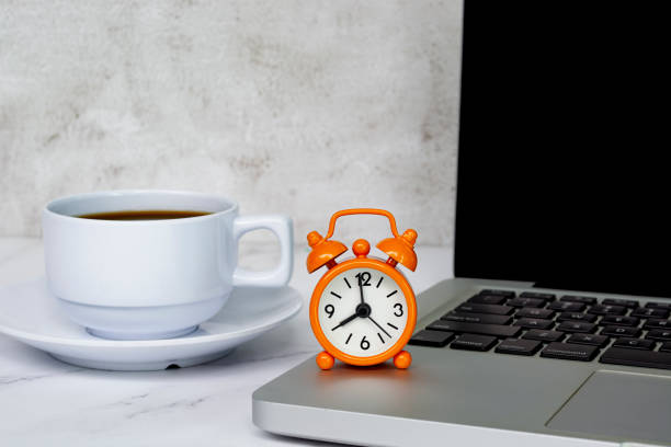 Alarm clock on laptop with coffee cup on a table. The clock set at 8 o'clock. stock photo