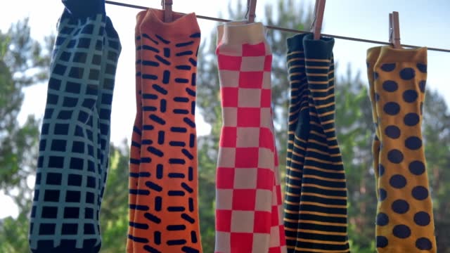 men's colored socks with bright different patterns are dried on a rope with clothespins. close-up.