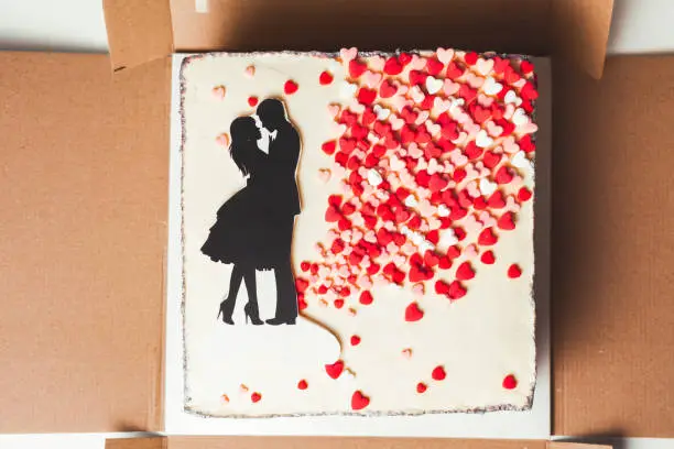 rectangular wedding cake with red hearts scattering and illustration of a loving couple on the white cream cheese frosting
