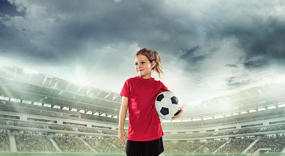Beginner football player in red uniform standing with ball at the open air stadium. Competition, game event. Concept of sport, competition, movement, lifestyle, childhood