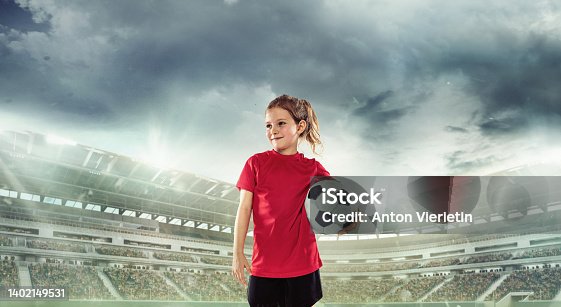 istock Beginner football player in red uniform standing with ball at the open air stadium. Competition, game event concept 1402149531