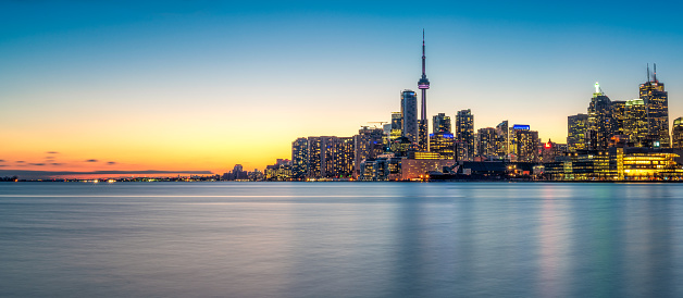 A panoramic view of Toronto's skyline, seen over the water at dusk.
