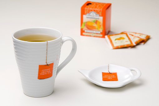 White ceramic illustrated mug with tea inside and saucer aside, with orange tea bag box at the background