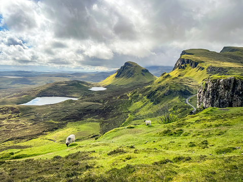 Quiraing hike in the Scottish Highlands on the Isle of Skye in Scotland. Green Spring and early Summer grass with blue and grey cloudy sky. Stony outcroppings carved by glaciers.
