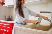 Close up of smiling woman fills up reusable water bottle in the kitchen