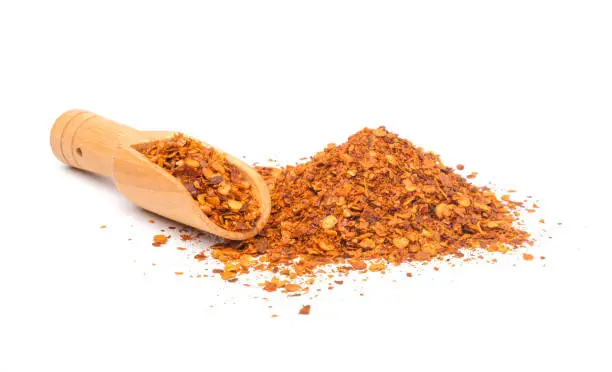 Crushed red cayenne pepper, seeds pile and wooden spoon isolated on white background.