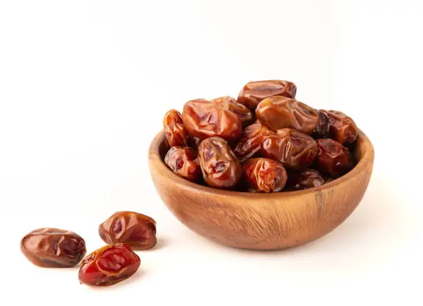 Dried dates in wooden bowl isolated on white background.