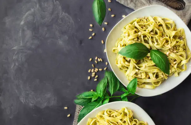 Fettuccine pasta with pesto sauce, basil and pine nuts on concrete background. Italian cuisine. Top view. Copy space area.