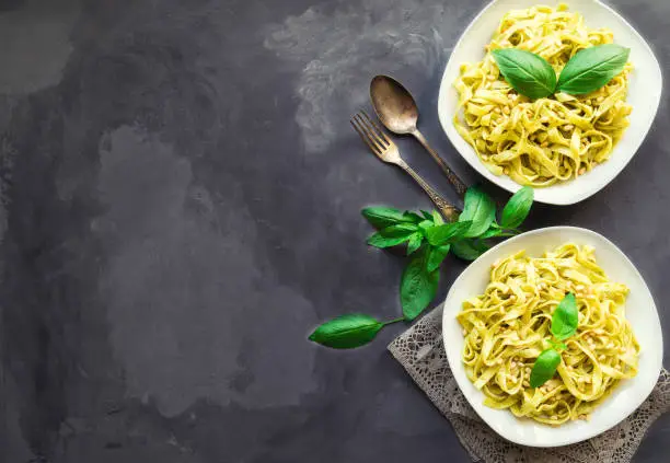 Fettuccine pasta with pesto sauce, basil and pine nuts on concrete background. Italian cuisine. Top view. Copy space area.