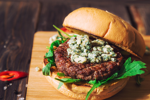 Fresh burger with blue cheese and arugula on rustic wooden background