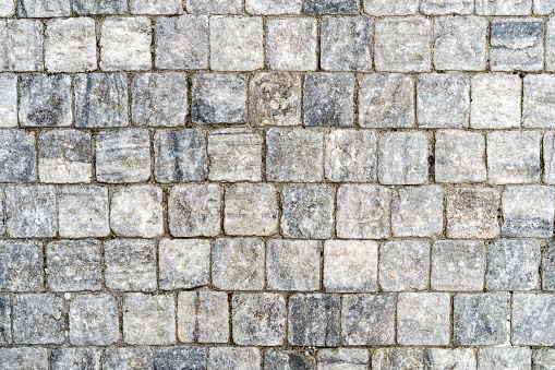 Granite cobblestone pavement, full frame of regular square cobbles in rows. Natural stone textured background
