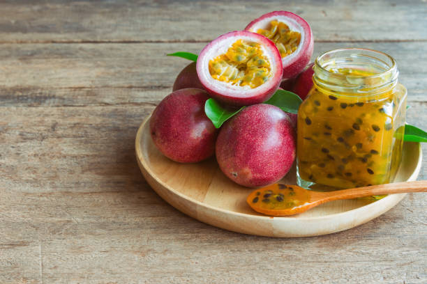 Homemade passion fruit jam in bottle on wood plate. Passion fruit jam on wood table in side view with copy space for background. Fresh passion fruit and homemade jam on wood table in natural concept. mermelada de maracuya casero en botella en placa de madera. mermelada de fruta de la pasión en la mesa de madera en vista lateral con espacio de copia para el fondo. maracuyá fresco y mermelada casera en la mesa de madera en concepto natural.