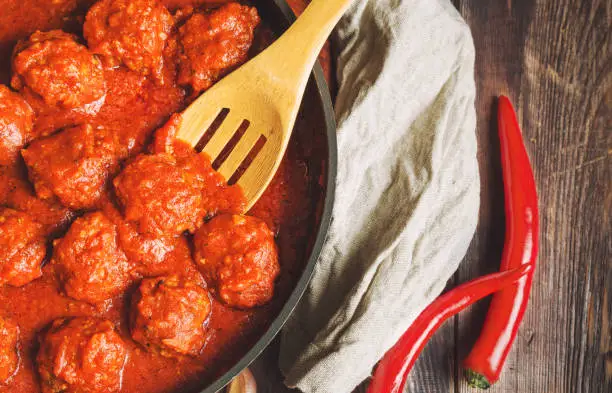 Meatballs with tomato sauce in cast iron skillet on rustic wooden background. Top view.