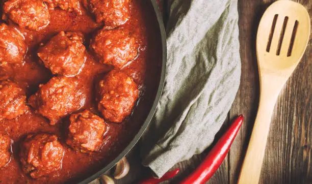 Meatballs with tomato sauce in cast iron skillet on rustic wooden background. Top view.