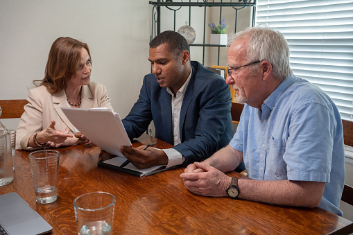 Financial Advisor Pointing Out Options To A Mature  Woman Client As Her Husband  Listens Intently