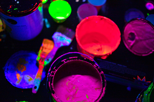 A scene of glow in the dark paint cans, brushes and splashes of paint.