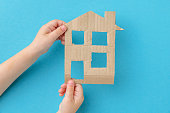 Children's hands holding a cardboard house on a blue background.