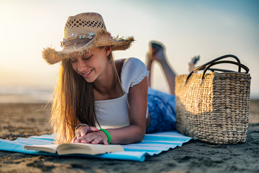 Teenage girl on the sandy beach. The girl is enjoying reading a book.\nCanon R5