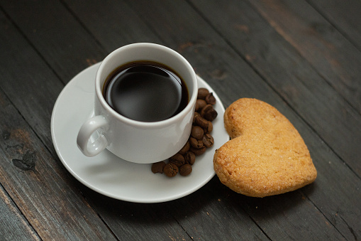 a cup of coffee with coffee beans and love cookie on wooden surface.Valentine day holiday.